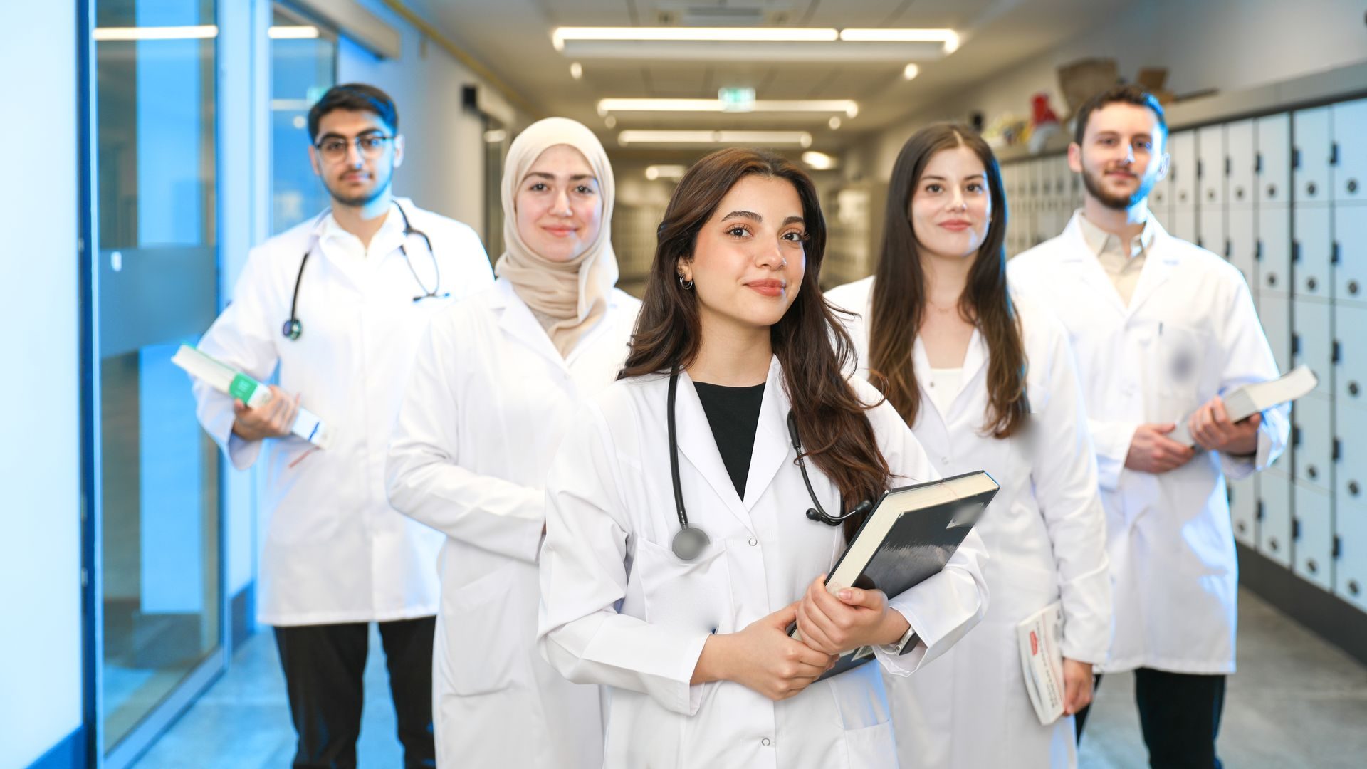 Cinq étudiants en médecine et en pharmacie, en blouse blanche, livres à la main, dans un couloir de leur faculté.