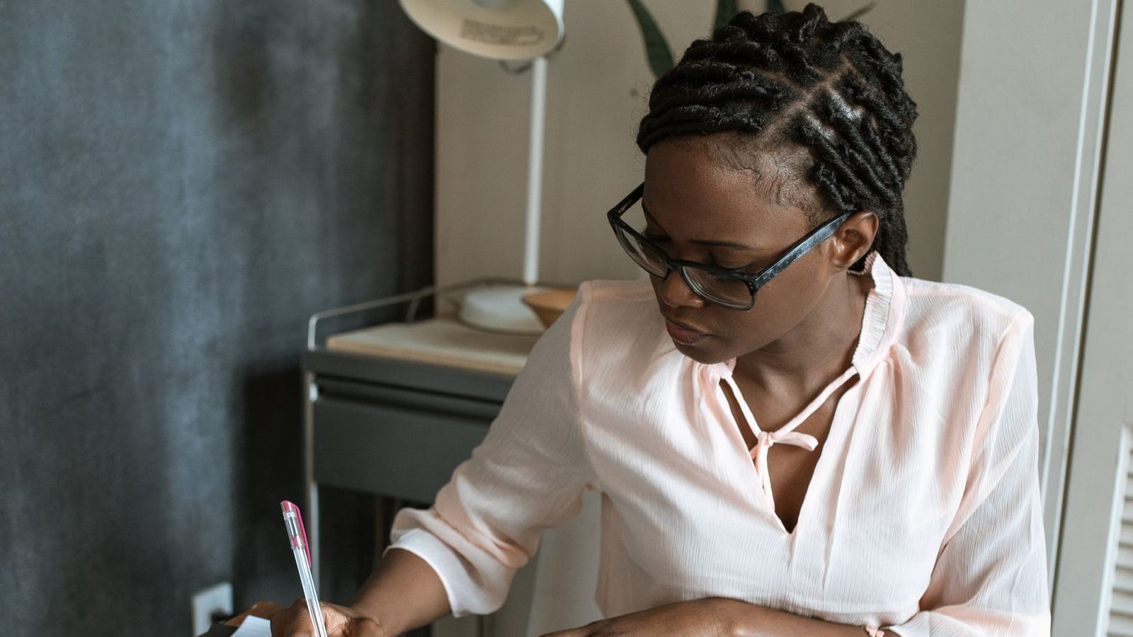 Une femme à lunettes prend des notes à son bureau.