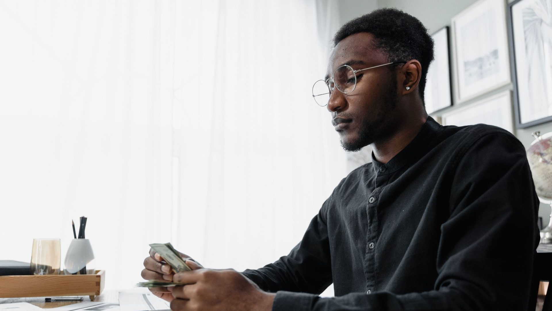 Un homme à lunettes compte des billets à son bureau, l'air concentré.
