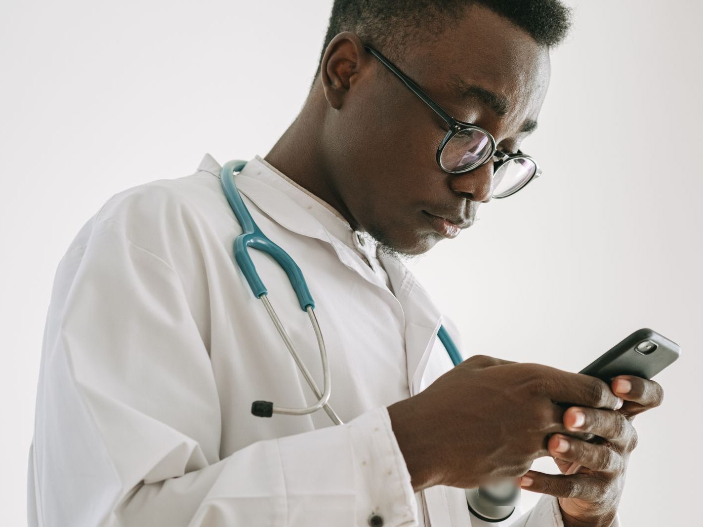 Un médecin en blouse, stéthoscope au cou, cherche sur son téléphone la pharmacie qui a le médicament prescrit.