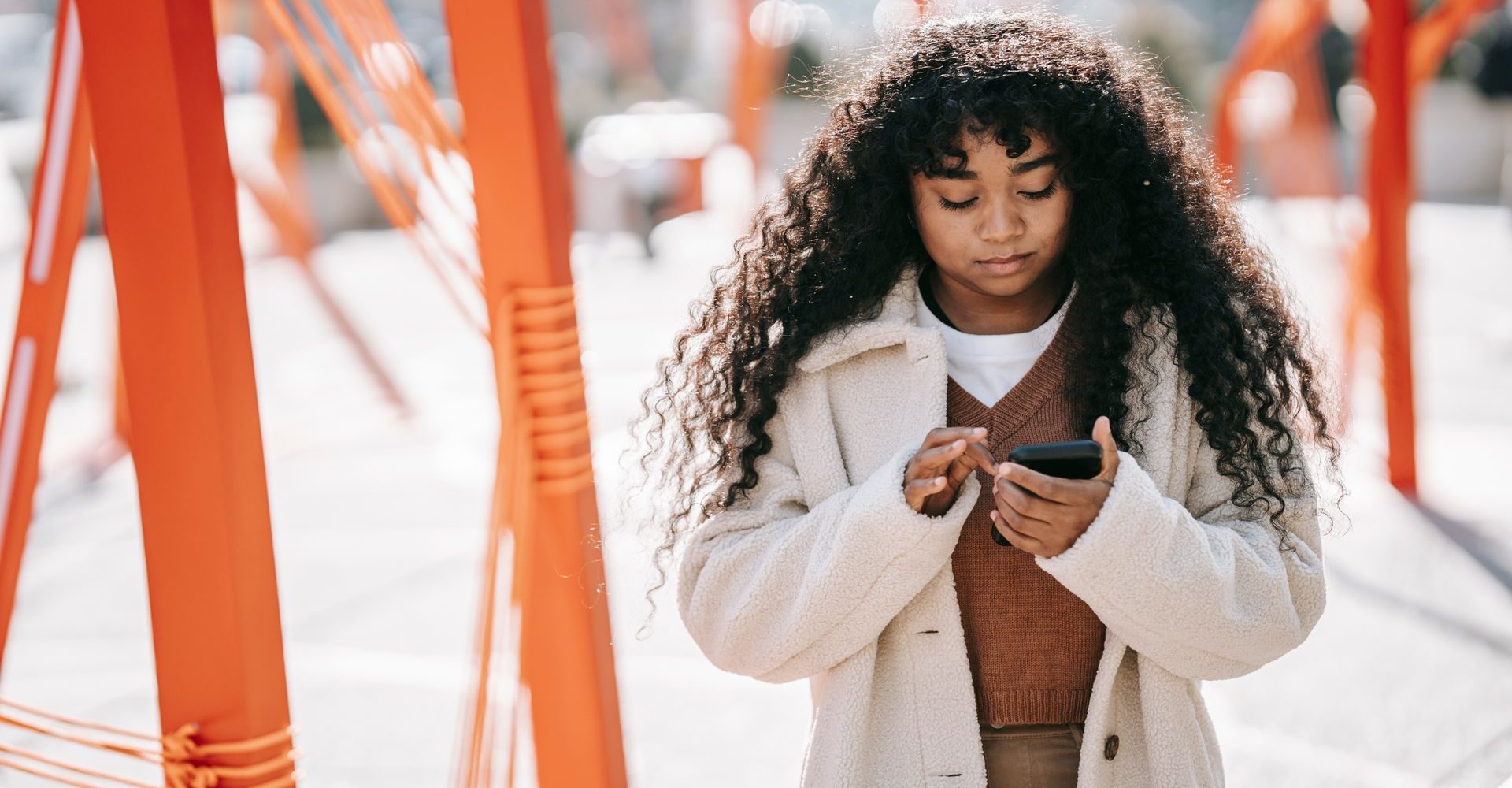 Dans la rue, une jeune femme regarde son téléphone : elle cherche où trouver son médicament.
